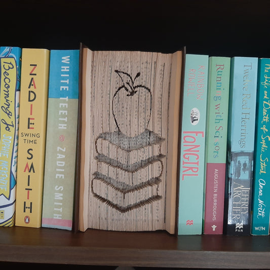 A book fold with a picture of a pile of books with an apple on top on