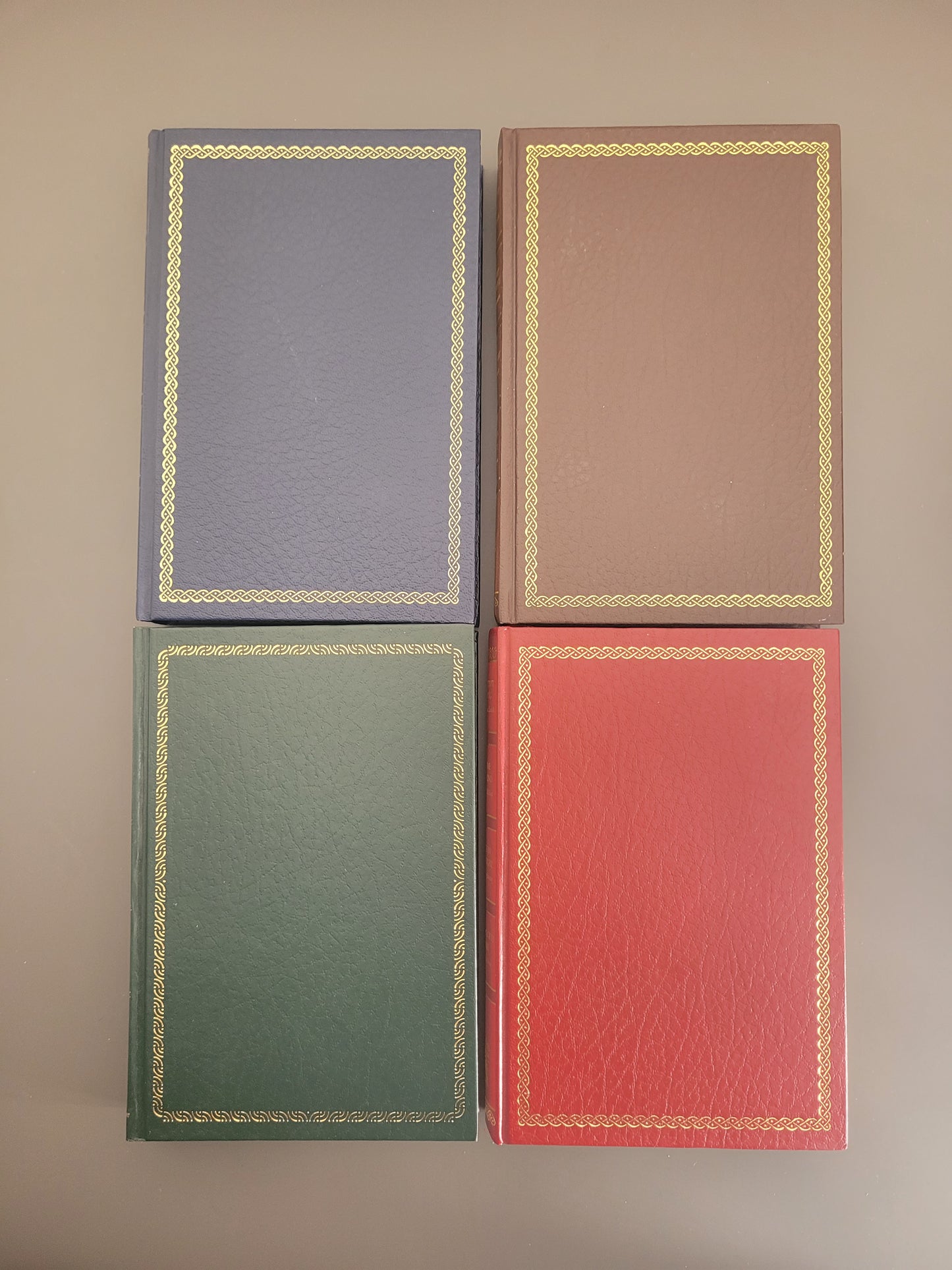 A picture of 4 hardbacks - one blue, one brown, one green and one red.