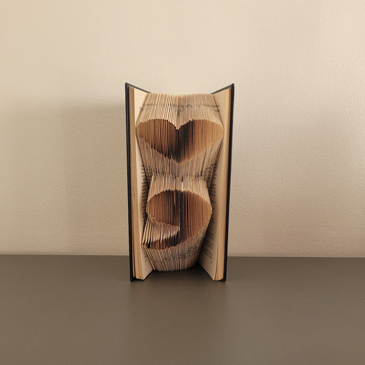 A photo of a folded book art with a heart semi colon on the front.