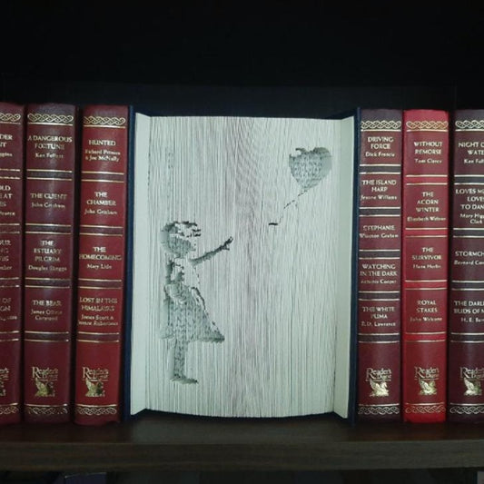 A Book Fold Art piece showing the Banksy image of "A girl with heart balloon" on the front