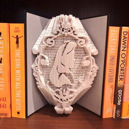 A Book Fold Art showing an Alice in Wonderland silhouette on, with a swirly border.